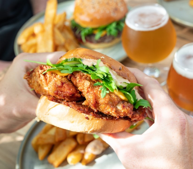 Close up of a burger being held, with chips an a beer in the background