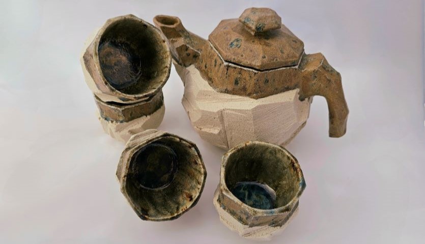 A hand-crafted set of pottery in neutral brown and tan colours, with four cups and teapot.