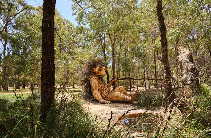 Giant wooden sculpture in a small bushland clearing leaning against a tree
