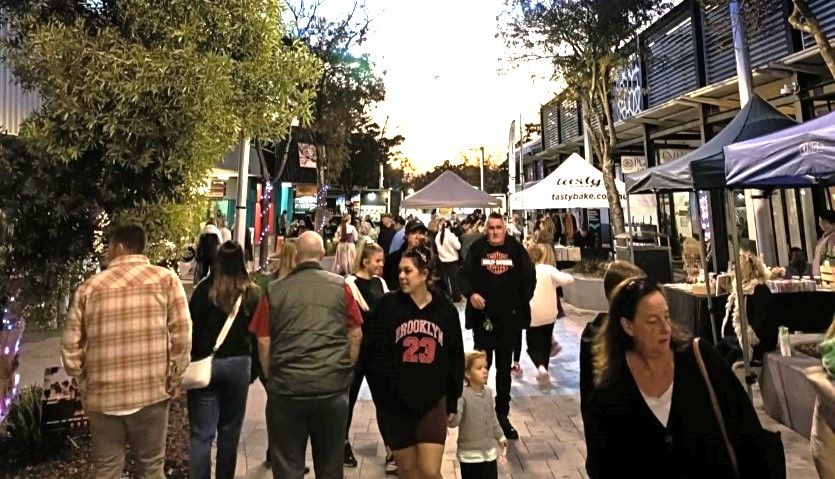 Night markets on a pedestrian mall with dozens of people looking at market stalls and a sunset behind them