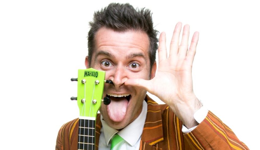 A man with a silly expression and his tongue sticking out, holding a green guitar