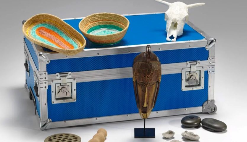 A blue and silver case is surrounded by various 3D artworks, including an animal skull, some woven baskets and a tribal-style mask.