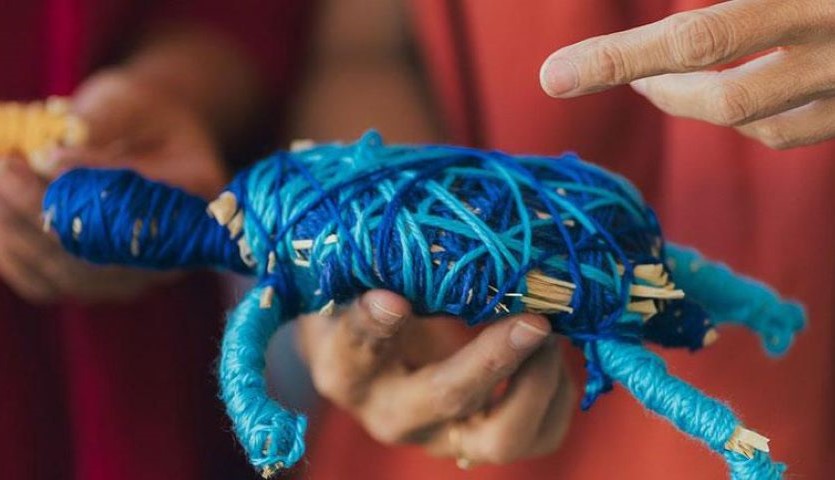 A close-up image of a blue, woven turtle made of wool and natural fibres