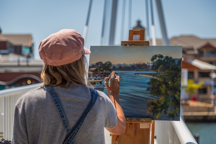 Artist painting on a canvas outside along a foot bridge