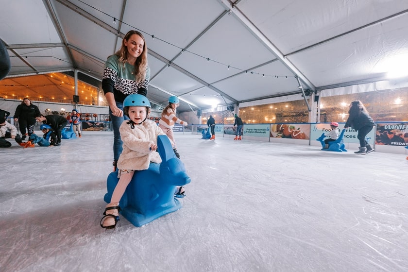 Mother pushing young daughter on 'kanga' ice skating aid.