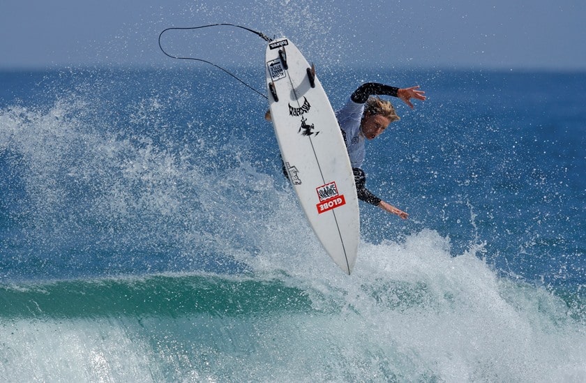 Male surfer with a white surfboard, getting air off a wave 