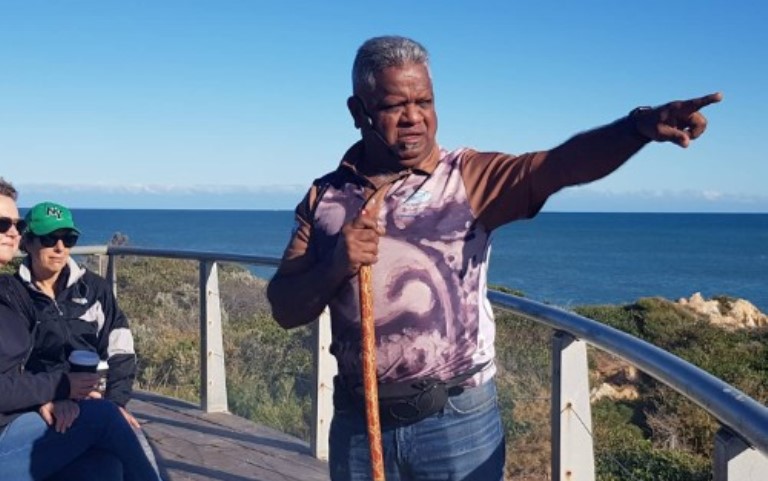 Aboriginal man holding a stick and pointing to the landscape.
