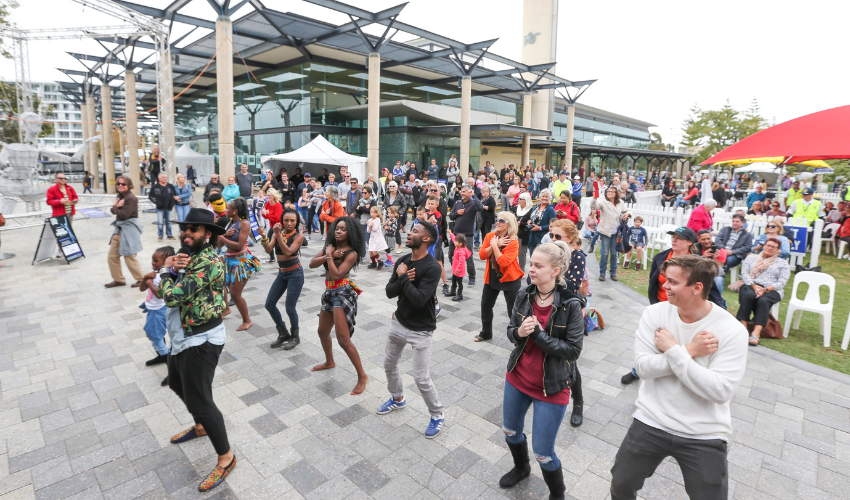 Camera facing a large crowd of people copying the dance moves from a professional performer