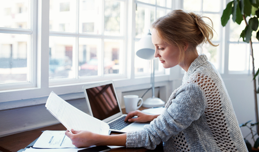 A young lady sat at her desk, studying documents with her computer open