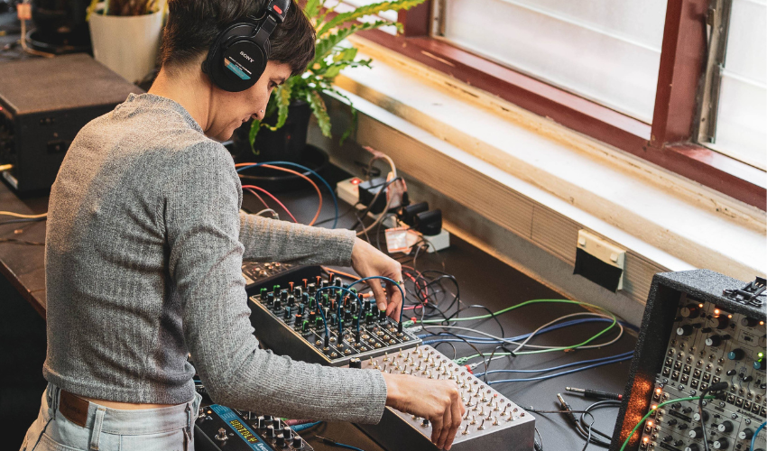 A musician wearing headphones is leaning over a mixing desk
