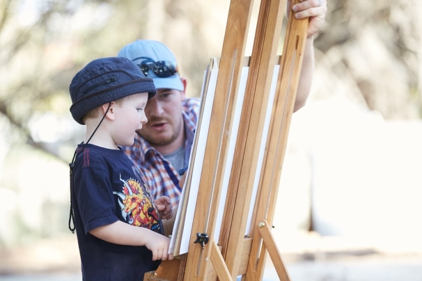 Father and son looking at a painting easel and canvas outside