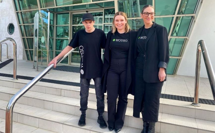 Three people standing on a set of stairs out the front of an office building. Everyone is wearing black clothing with the logo ‘WOTSO’.