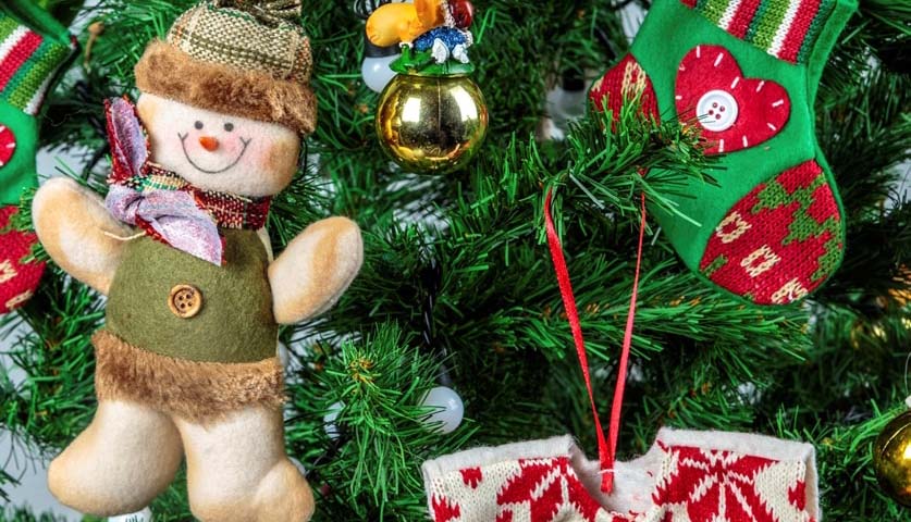 A bear, stocking, shirt and bauble hanging on a green Christmas tree