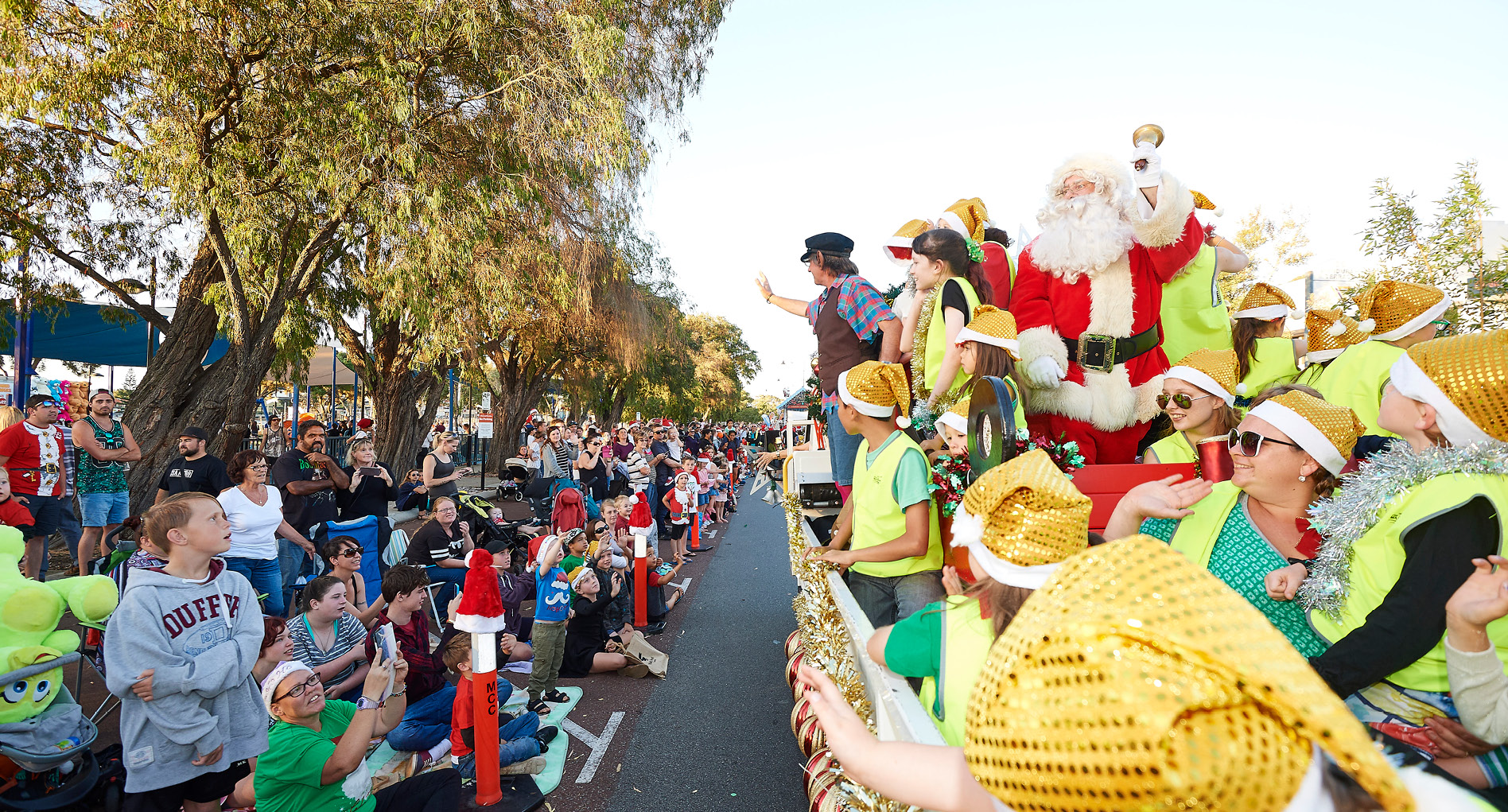 Santa and his elfs riding on a float with members of the public dressed in Christmas dress up watching on from the side of the road