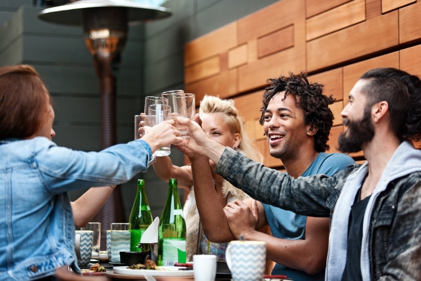5 x people clinking glasses over a table with food and cups.