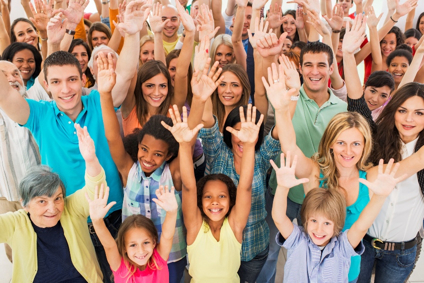 Large group of people of all ages with both hands up in celebration