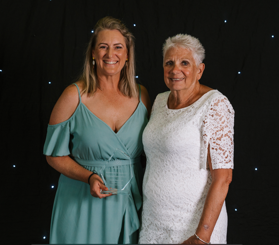 Two women side by side with sports awards trophy