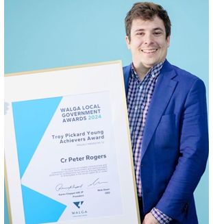 Cr Rogers stands smiling with award