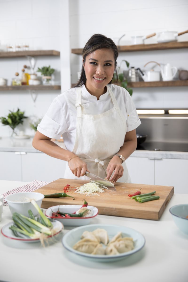 Diana in the kitchen, chopping food and looking at camera smiling