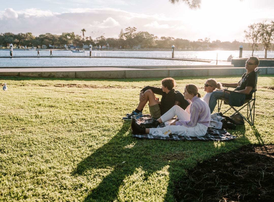 Family sits on foreshore with water and sunset in background