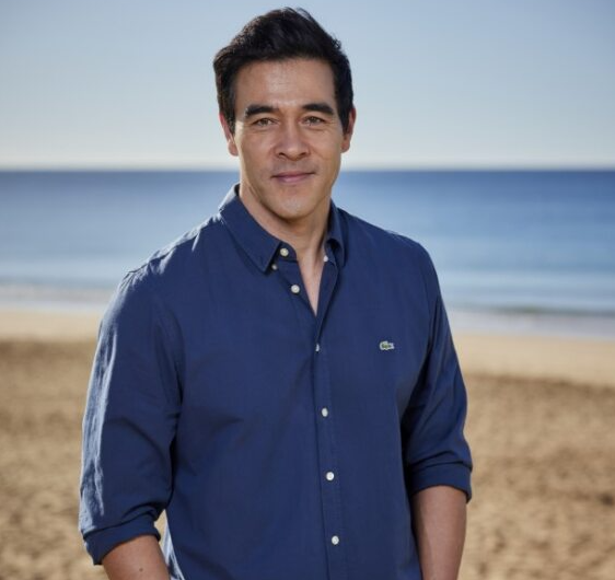 Male stands and looks into camera, beach background