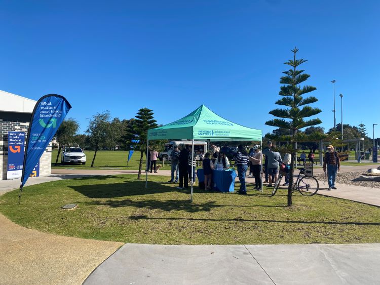 Group of people providing feedback under and around a shade tent at the Mandurah Matters Big Check-in outdoor pop-up event held at the Mandurah Skate Park