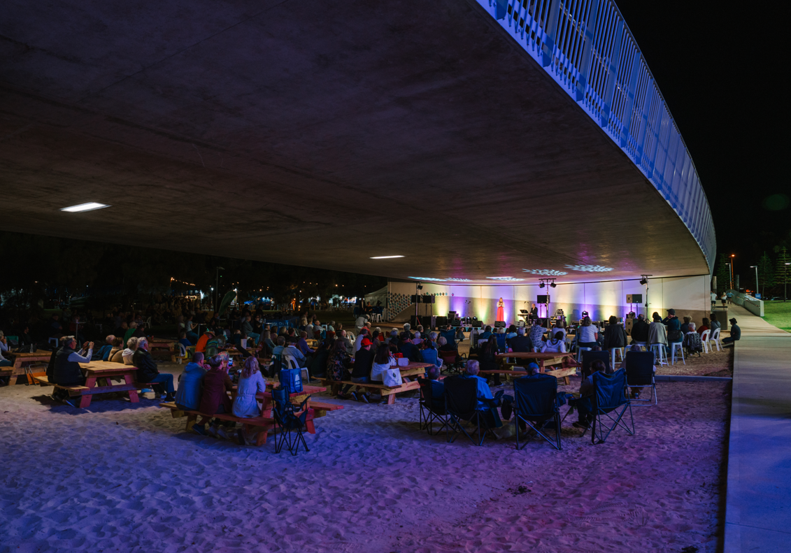 Groups of people sitting underneath Mandurah Bridge during a night time concert