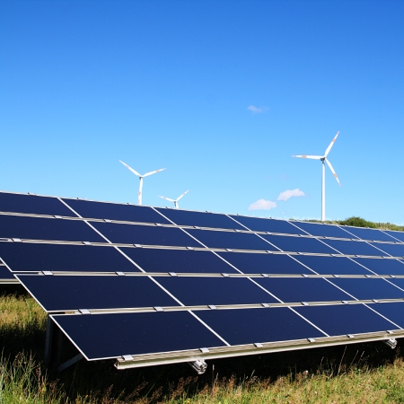 Solar panels with wind turbines in the background.