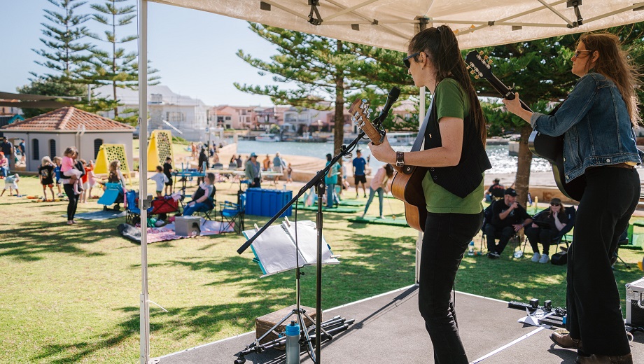 Two musicians playing acoustic guitars on stage at a community event