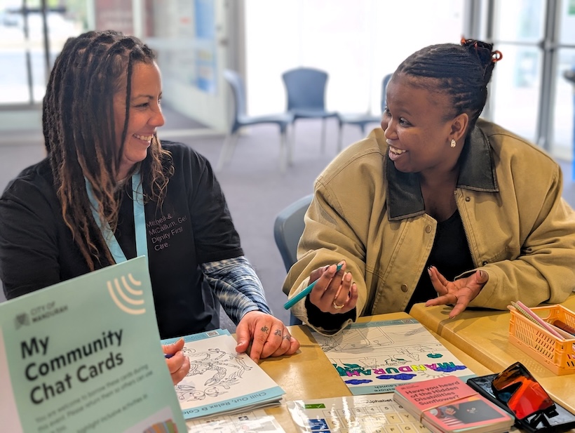 Two people at a network meeting sit together at a table, talking and smiling while colouring in a mindful colouring sheet.