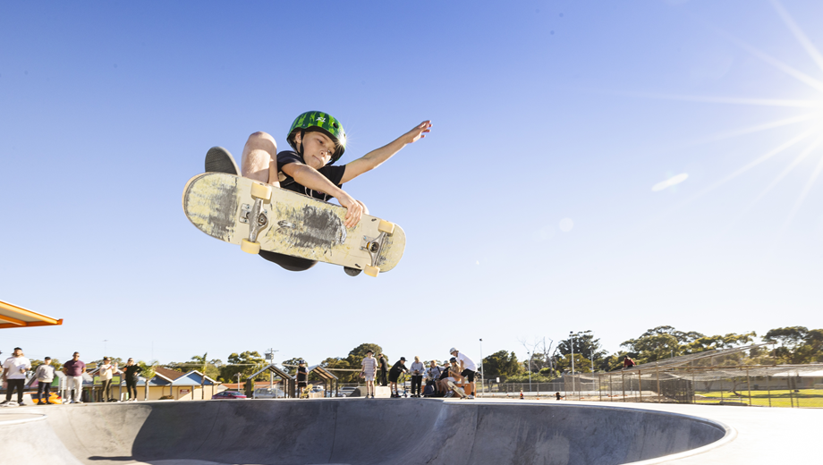 Young boy on skateboard jumping up and doing a trick at a skatepark.