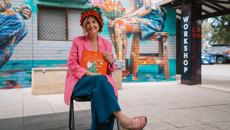 Mayor Amber Kearns sitting in front of a mural at the CASM building with a Christmas book in her hands