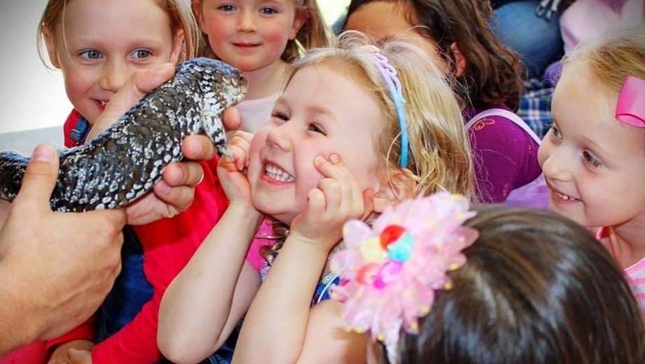 A group of kids looking at a bobtail lizard with one little girl excitedly smiling and holding her hands up to her face.