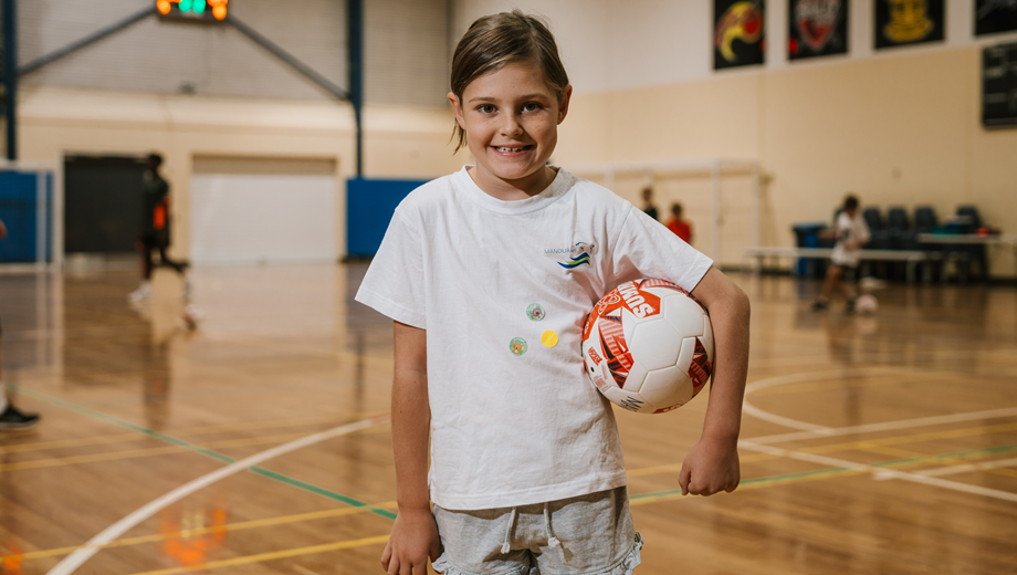 Young girl holding a futsal ball under one arm, standing on the MARC basketball court.