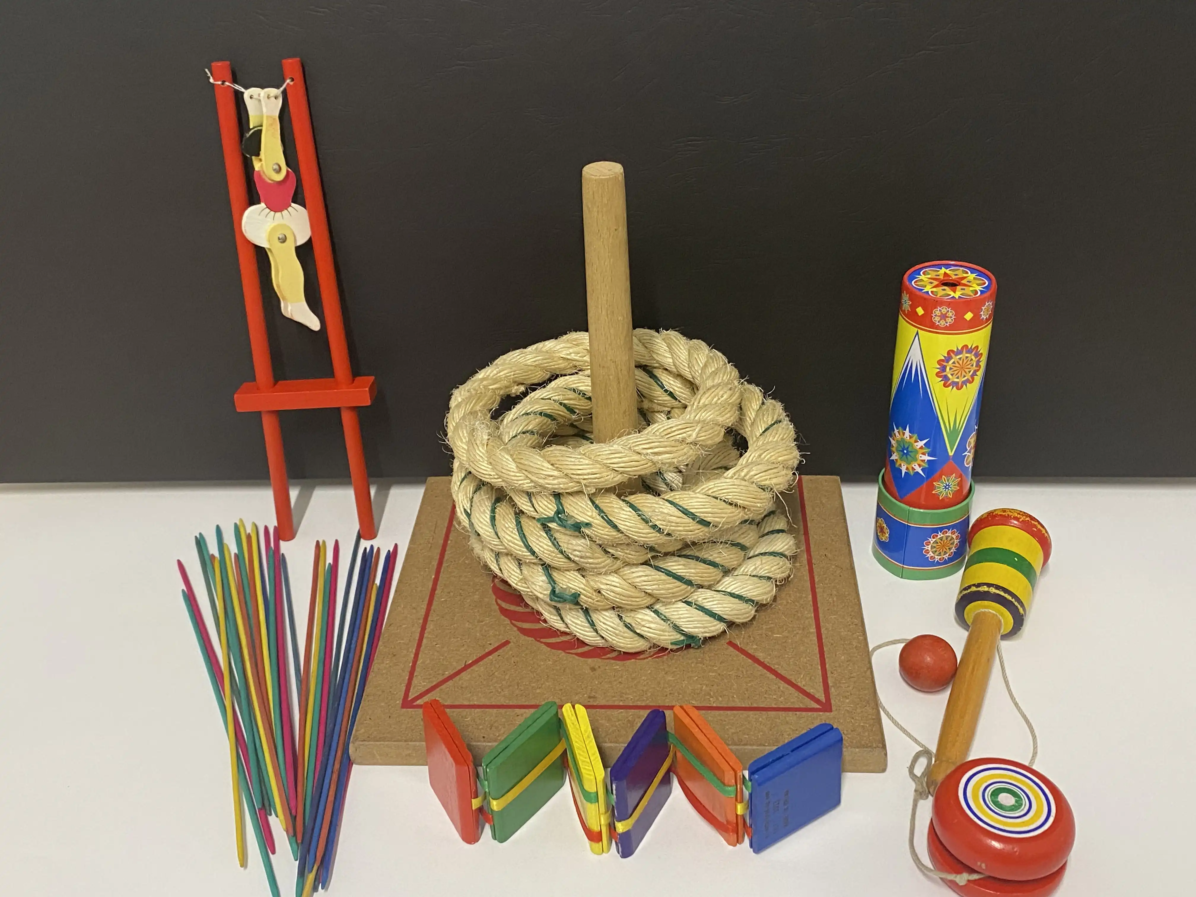 A selection of colorful vintage children’s toys, including a ring toss set, pick‑up sticks, a spinning top, a clap toy, a kaleidoscope, and a small red balance toy.