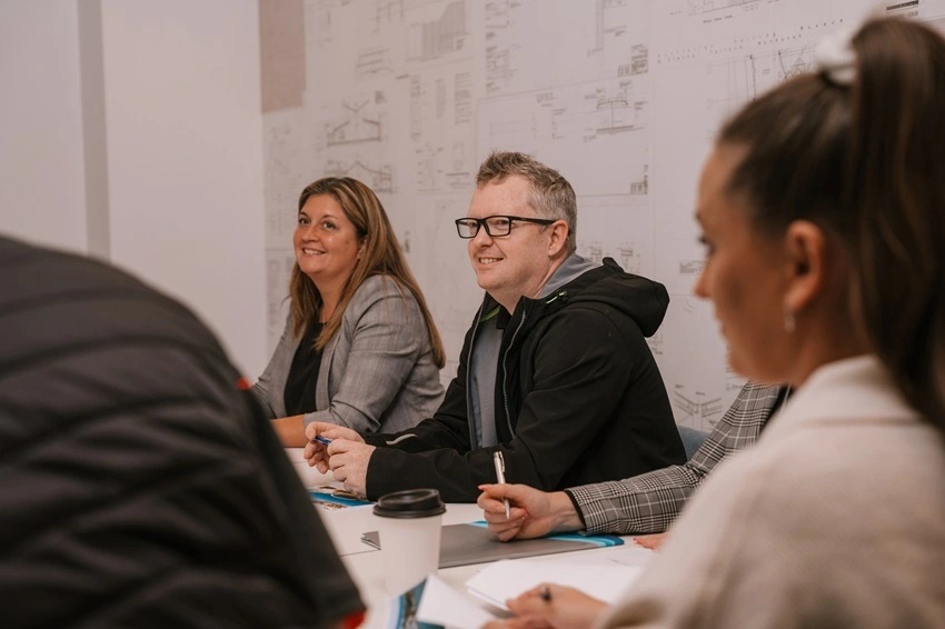 People sitting at desk with pens and paper listening at workshop event.