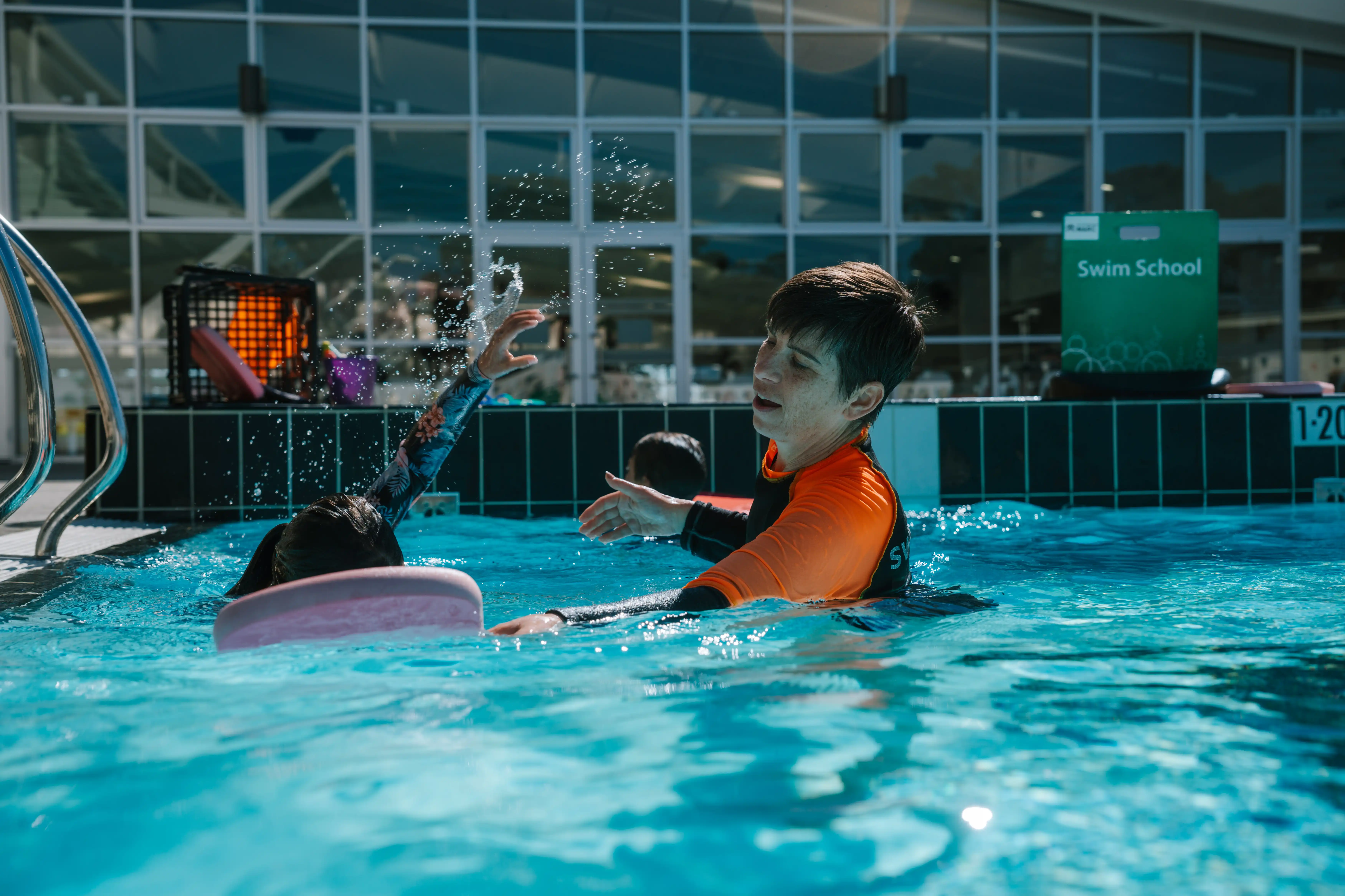 Child doing freestyle in swim lesson with swim teacher in outdoor pool.