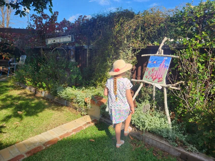 Young person with hat on viewing art set up in a sunny garden.